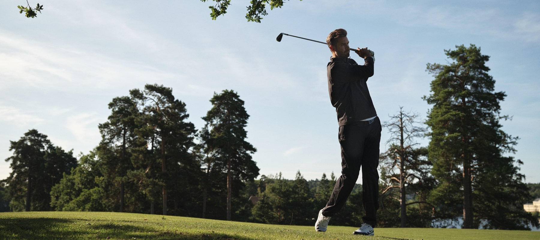 Male golfer wearing black rain gear swinging on a sunny autumn day