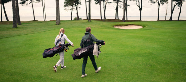 Male and female golfers walking on the golf course carrying golf bags.